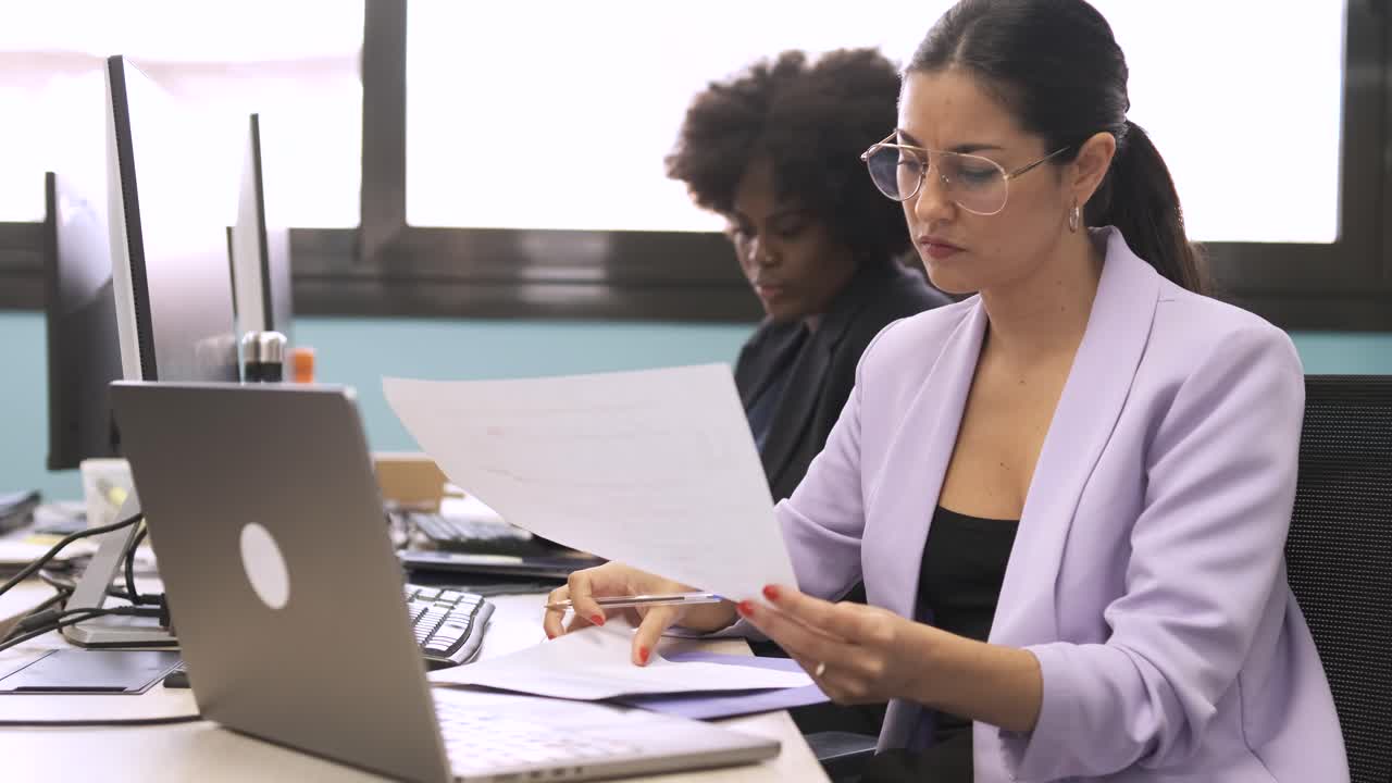 Busy businesswoman analyzing data on documents at computer desk