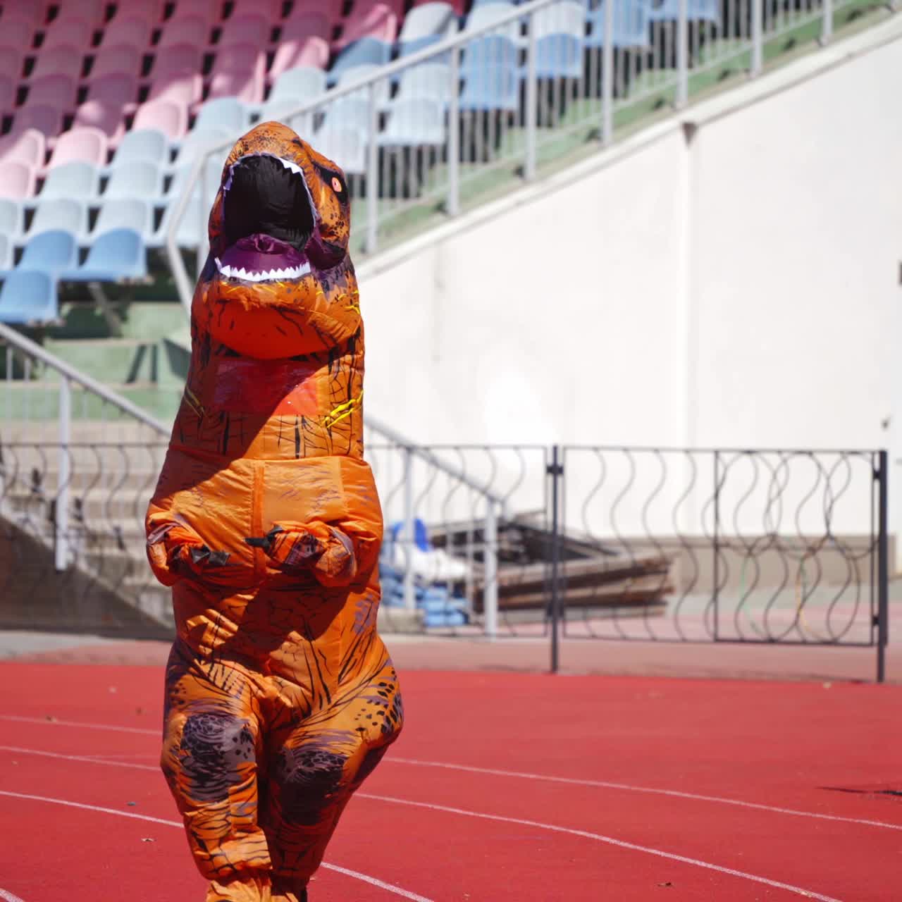 Big dragon in blow-up costume. Person dressed in funny orange costume walks on stadium in a sunny day.