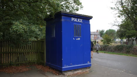 people walking past a blue emergency police box at a park