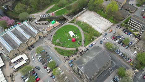 sweeping drone shot of todmorden town centre markets and carpark , with a community garden right next door , lovely old buildings and a bustling scene