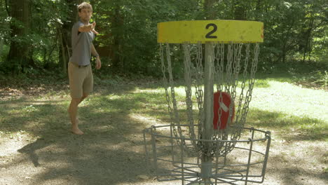 man scoort een basket in een rondje discgolf in het bos en viert feest in slow motion