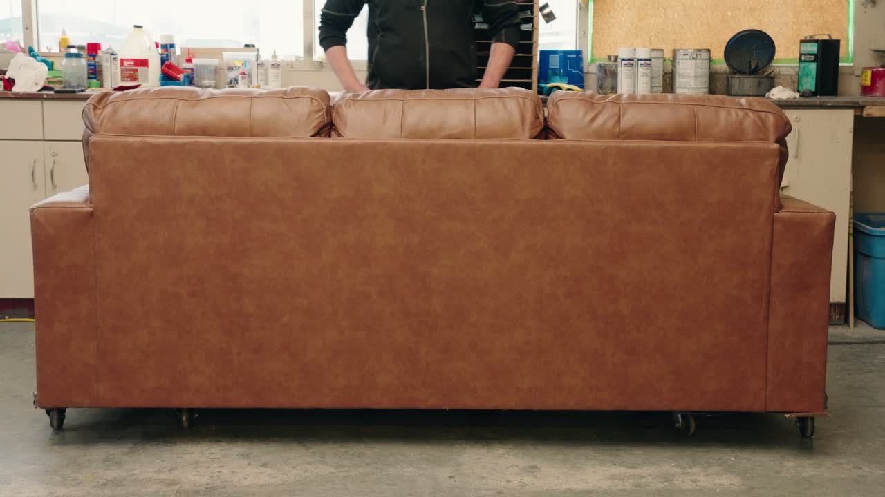 Brown leather sofa back in workshop as technician steps behind for pose