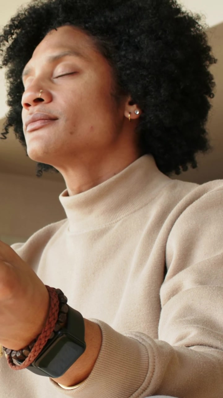 Vertical video: Camera starting man closing eyes, shifting left at home, showing tan turtleneck