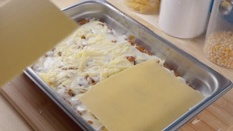 medium shot of adding pasta sheets to cheese, bechamel sauce and tomato sauce in a baking tray for making lasagne