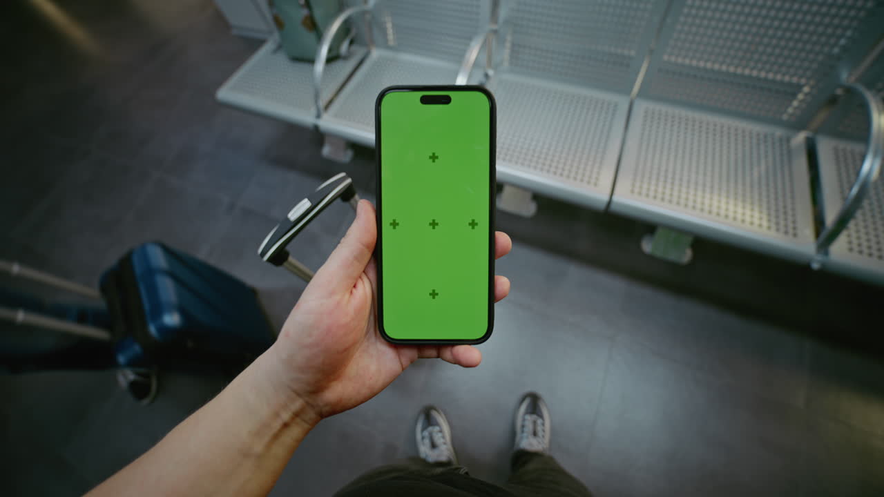 Person holding a phone with a green screen in a train station waiting room