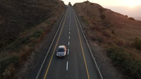 aerial view facing a car driving down from the highlands of golan heights, sunset in israel - tilt, drone shot