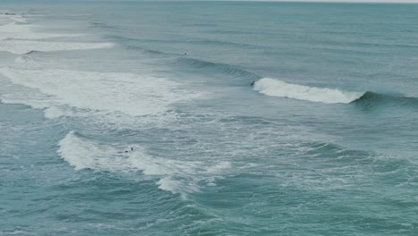 Rolling-Waves-in-Ocean-with-Surfers-in-Water-Waiting-for-Large-Tide,-Summer-Day