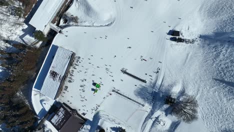 high altitude top down shot of bottom of ski run, ascending shot of skiers arriving at base of mountain lining up for the chairlifts