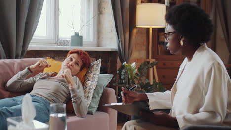 woman lying on sofa and speaking with psychologist during therapy session