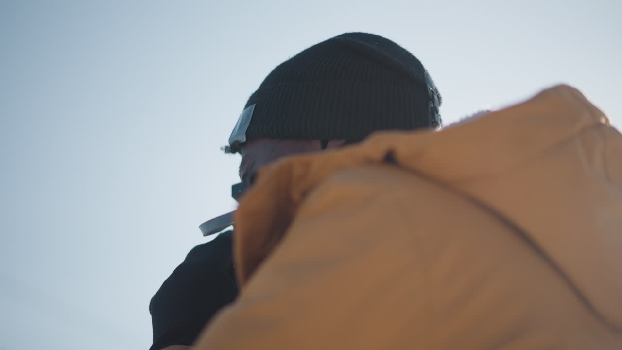 lower round view of freelance photographer peering through viewfinder gloved hands adjusting focus dial under clear urban winter sky bright sunshine over snowy street scene capturing details