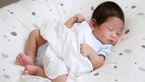 panning over a newborn baby from the left to the right side of the frame as it is sleeping on a soft mattress inside a crib