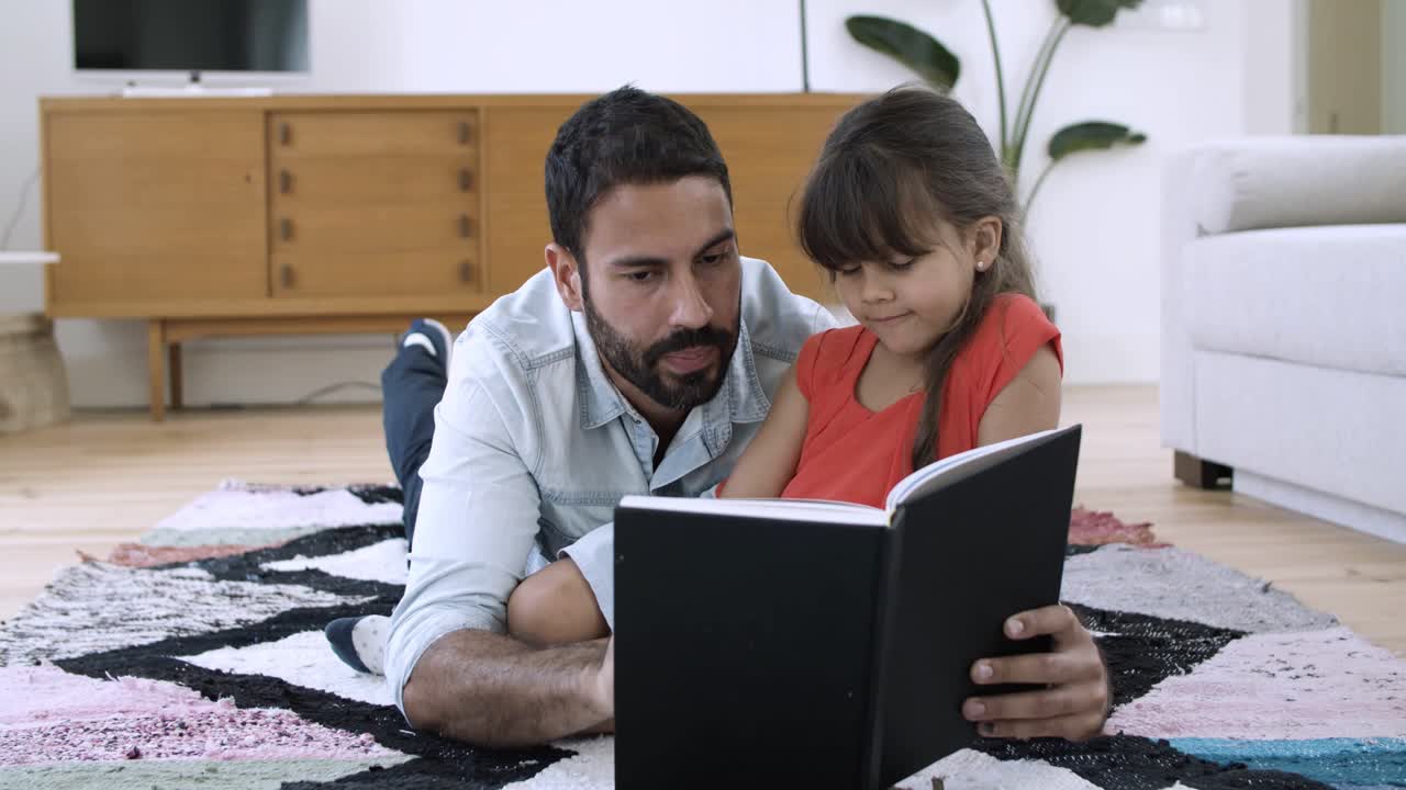 niña pequeña y su padre relajándose en el suelo y leyendo un libro