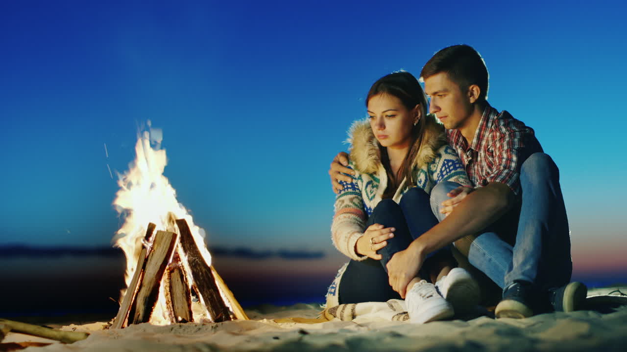 해변 모닥불에 앉아 있는 낭만적인 젊은 부부