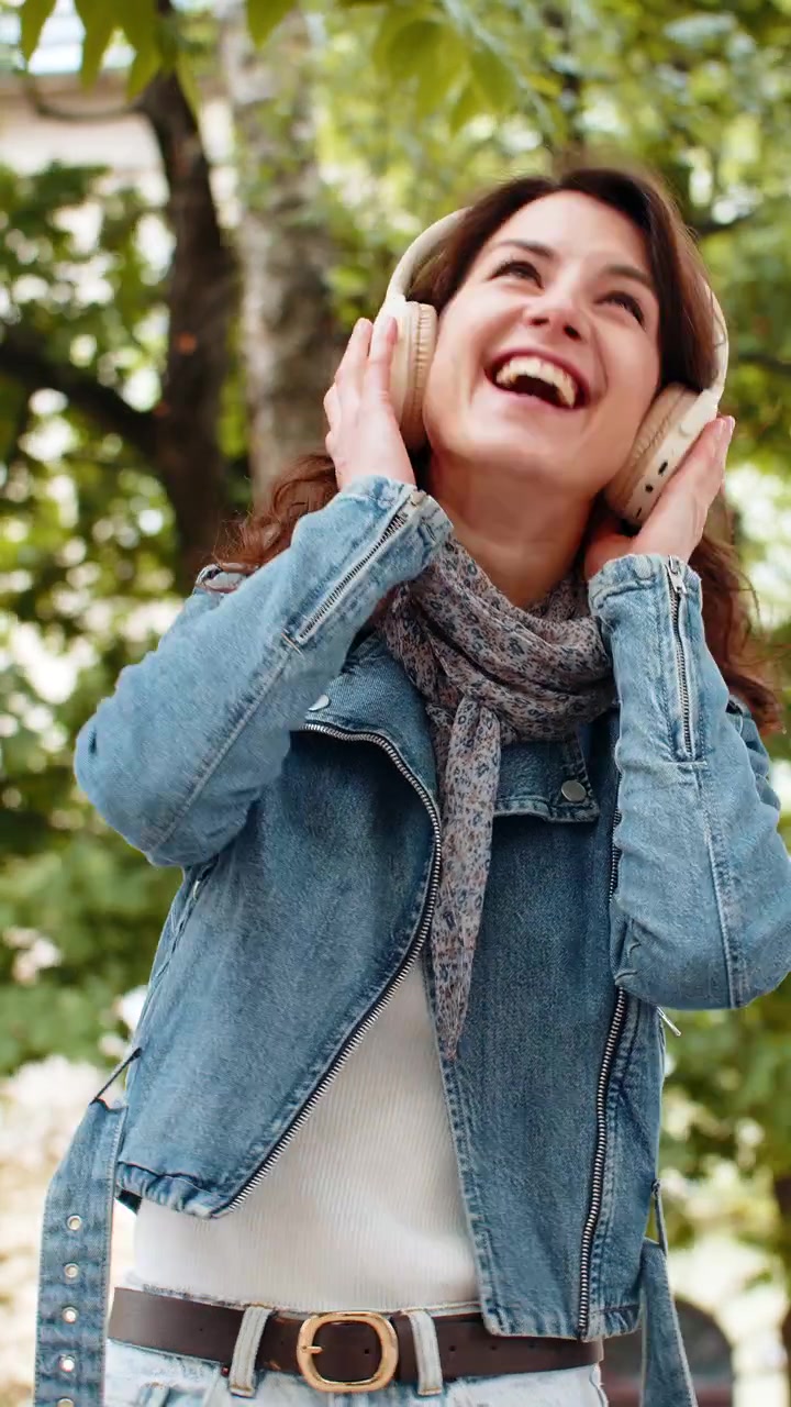 Joven sonriente escuchando música con auriculares, paseando alegremente por una calle urbana al aire libre.