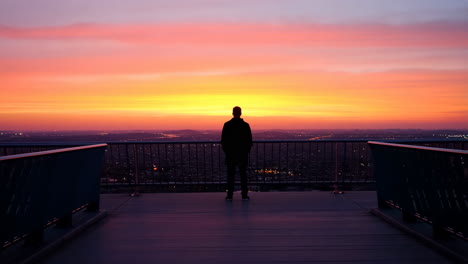 Man silhouetted against a vibrant sunset overlooking city lights