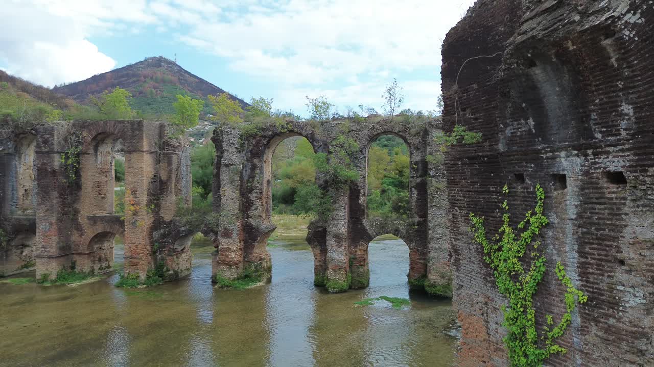 Rivelazione cinematografica con drone da un antico muro di mattoni agli archi monumentali dell'Acquedotto Romano di Nicopoli in Epiro, Grecia, con muratura storica e paesaggio fluviale scenografico