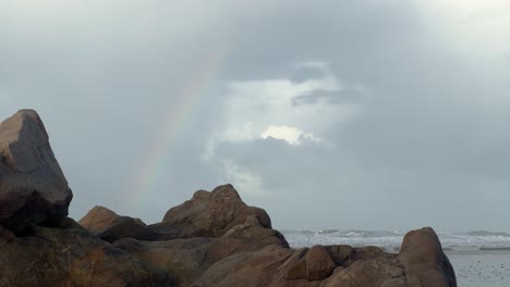 por encima de las tumultuosas olas del mar que chocan contra la escarpada y rocosa costa de zahara, un arco iris adorna el cielo, personificando el atractivo y las maravillas naturales del paisaje costero.