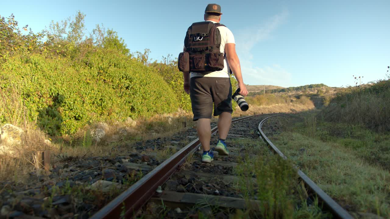 joven fotógrafo caminando sobre una vía férrea abandonada bajo el sol
