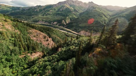 drone aéreo fpv volando sobre las exuberantes montañas del bosque verde de alaska y cañones rocosos y bajo el viejo puente de tren de metal cerca del parque nacional denali con bengalas solares
