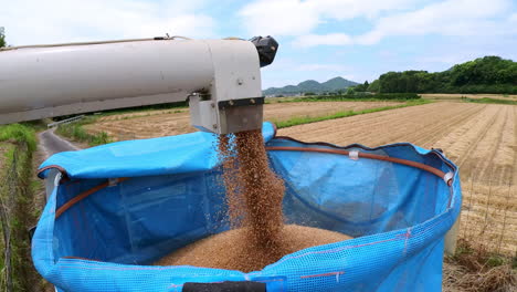 Harvester-unloading-wheat-in-rural-Japan,-under-a-partially-cloudy-sky