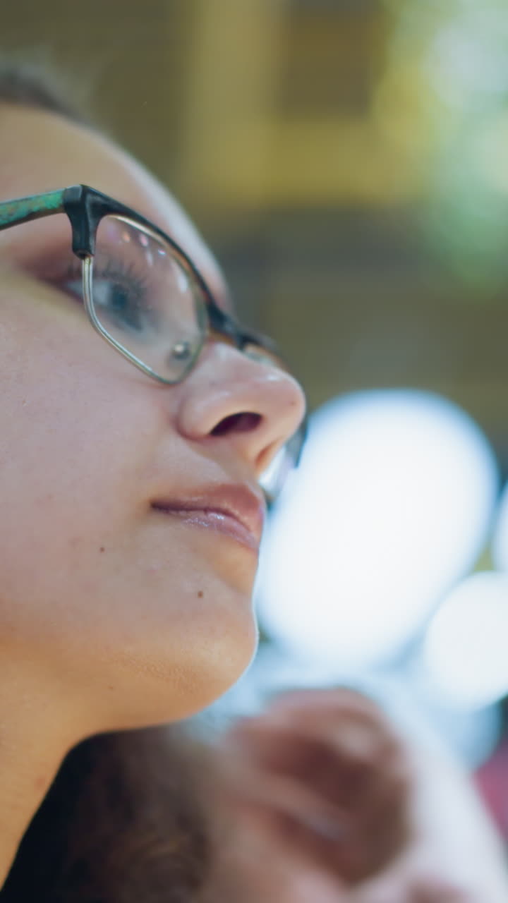 perfil de primer plano de una mujer con gafas, ajustando el cabello con una expresión serena, luces bokeh suaves y fondo borroso que proporcionan un ambiente suave, destacando un momento reflexivo