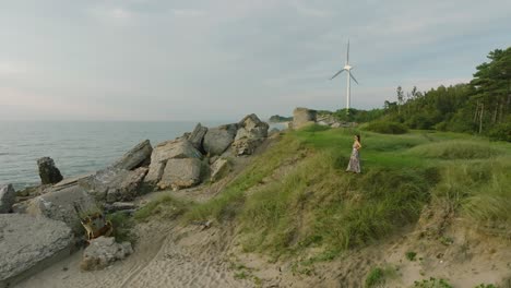 aerial establishing view of beautiful young romantic caucasian girl in a long dress on the white sand beach with old ruins, sunny summer evening, sunset, golden hour, wide drone shot moving back