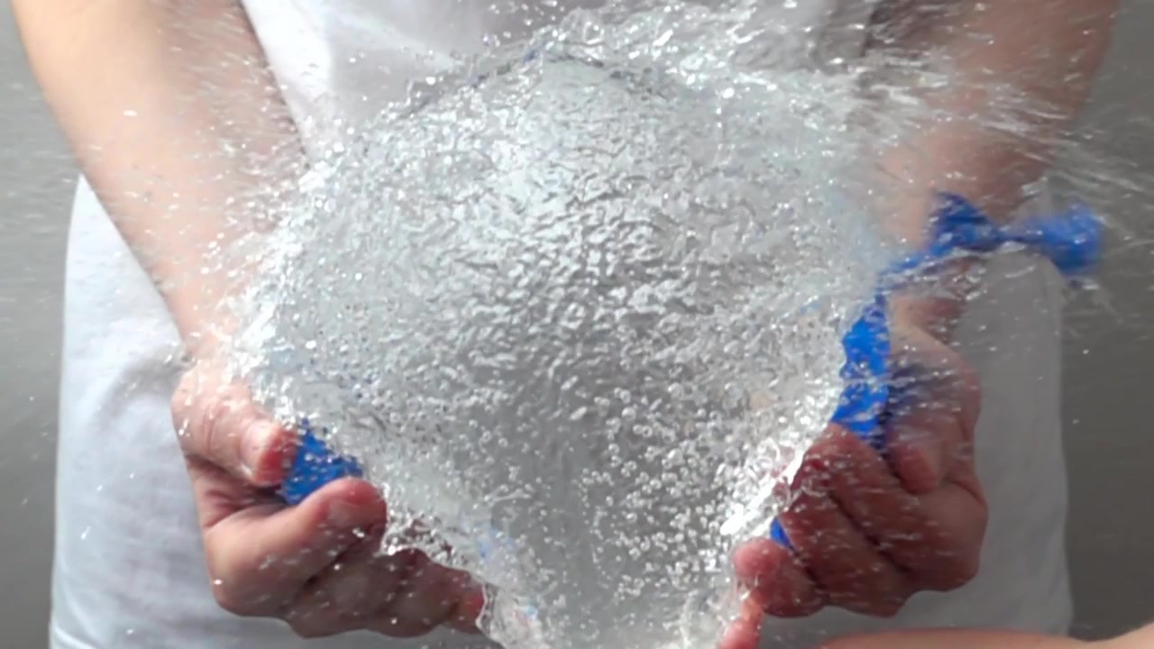 Un palloncino d'acqua nelle mani della ragazza. Rallentatore.