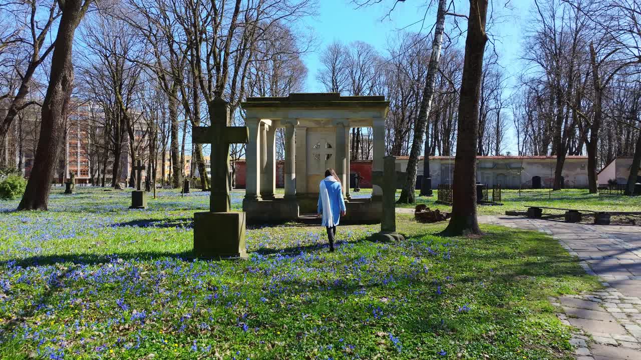 Young woman walks peacefully, Riga historic Lielie Kapi under spring trees
