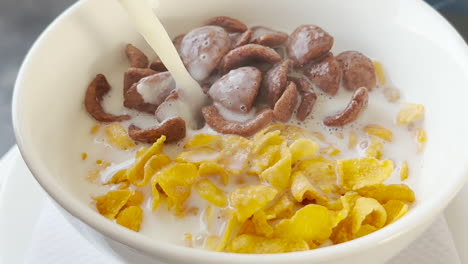 healthy breakfast concept - hand adds hot milk to a mixture of cereal and chocos from pot