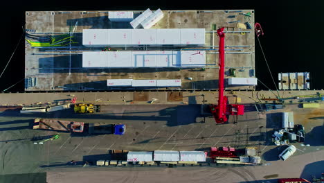 aerial timelapse, top down view of crane loading container ships on barge in sea water, high angle drone shot