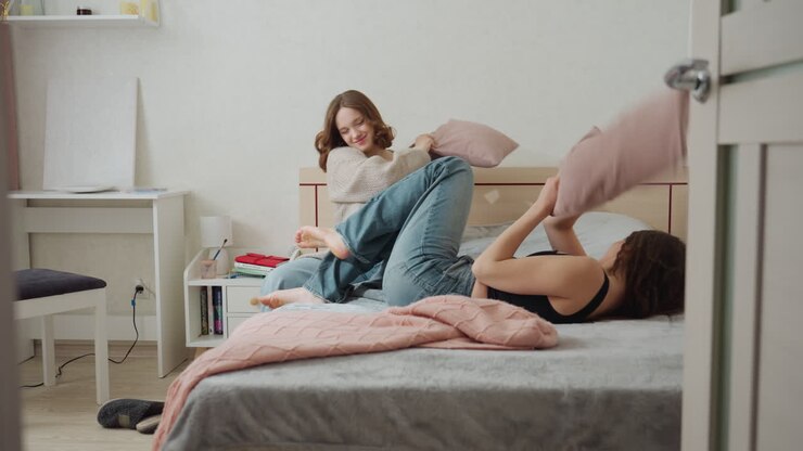 Divertente battaglia di cuscini, due donne che giocano a fare la lotta con i cuscini, risate e calci durante un'animata sessione di lotta con i cuscini, lotta con i cuscini spontanea e vivace tra due coinquiline allegre