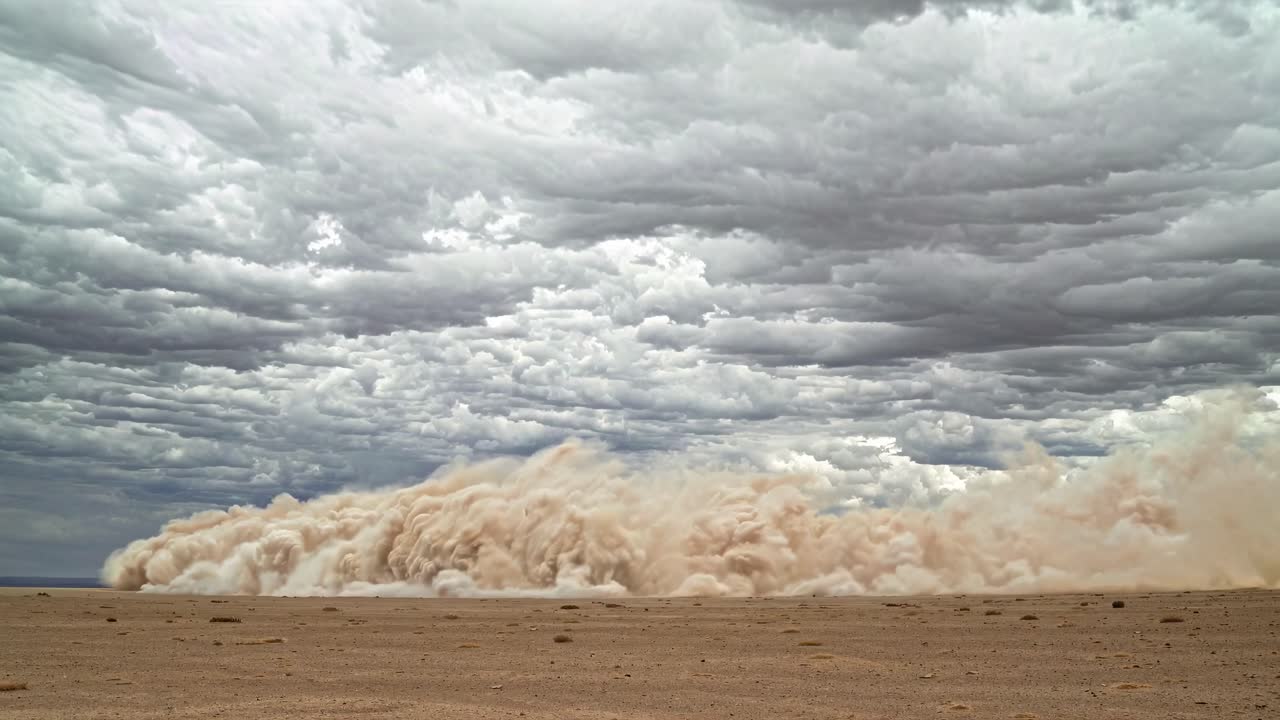 Wide-angle shot capturing a dramatic dust storm rolling across a barren landscape under a cloudy