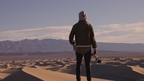 Video-En-Cámara-Lenta-De-Un-Fotógrafo-Encapuchado-Parado-En-Las-Dunas-De-Arena-Gritando-A-La-Gran-Distancia-Del-Cielo-Azul-Y-El-Vasto-Espacio-En-El-Valle-De-La-Muerte-Solo-En-California