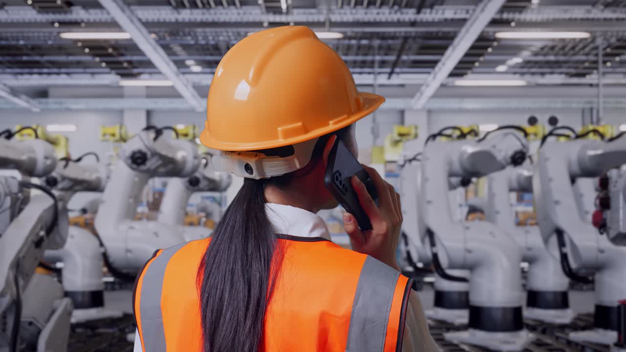 trabajador de la fábrica hablando por teléfono frente a los brazos robóticos