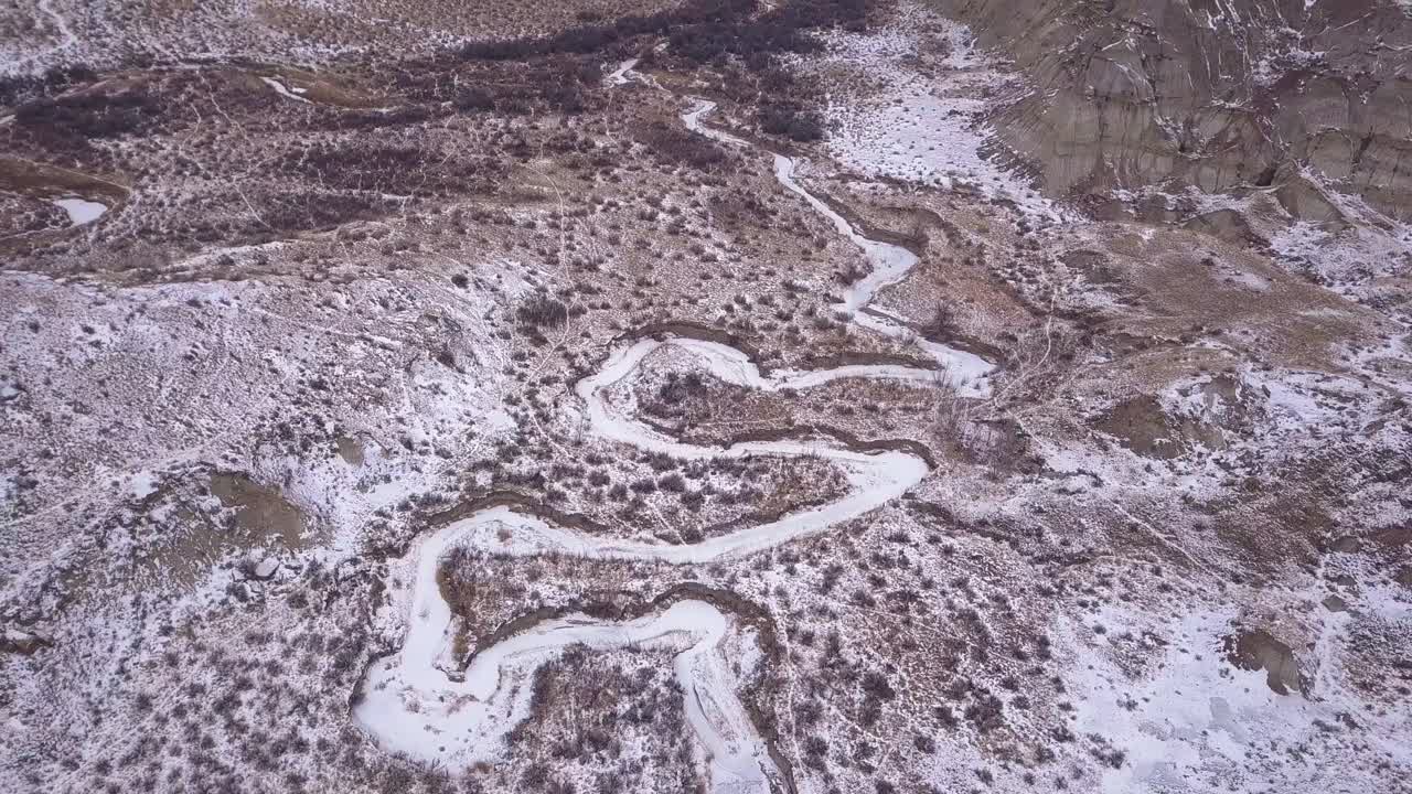 Flyover icy winter creek meandering thru valley bottom in badlands