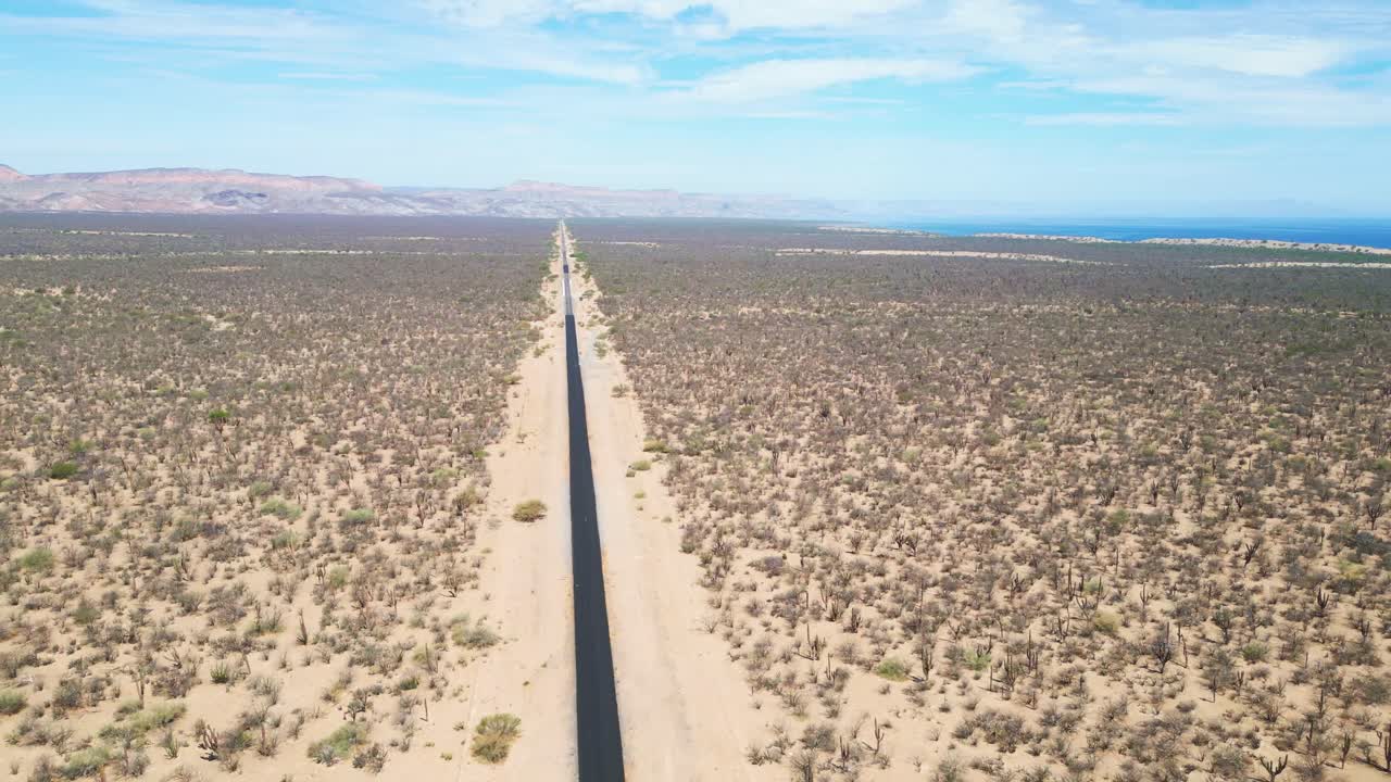 Long road stretching through the desert landscape with a view of the ocean in La Paz, Mexico