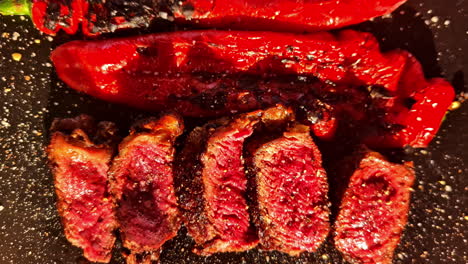 grilled medium-rare steak slices with roasted red peppers on black cutting board