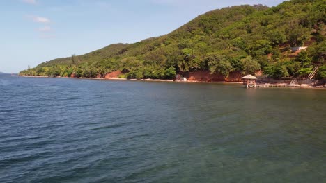 Vista-Aérea-Del-Día-Soleado-Con-Playa-Tropical-De-Arena-Blanca-Y-Agua-De-Mar-Turquesa-Clara-Con-Pequeñas-Olas-Y-Bosque-De-Palmeras