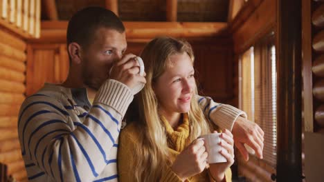 pareja caucásica pasando tiempo en casa juntos, mirando por la ventana, bebiendo bebidas