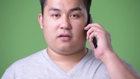 young handsome overweight asian man against green background