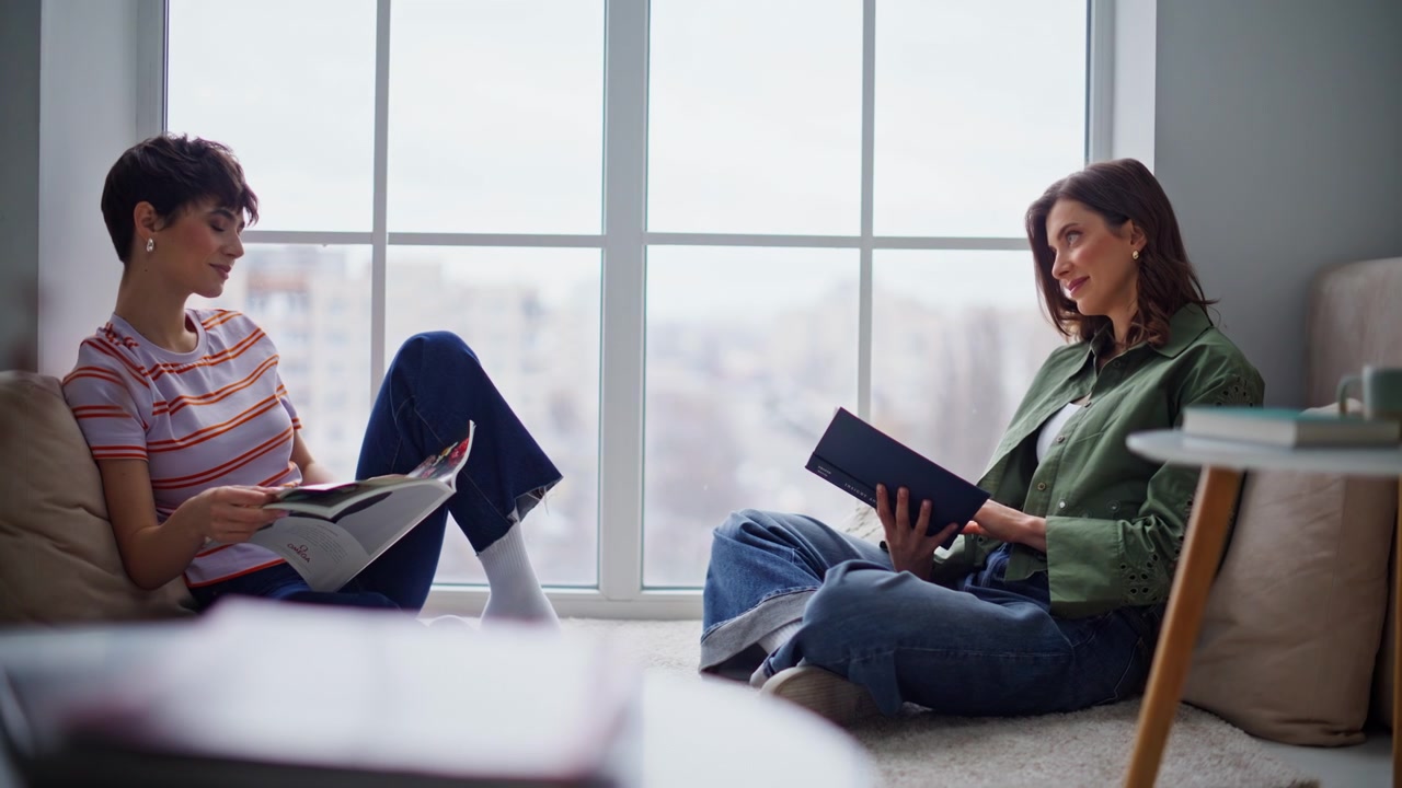 Two students reading home sitting by window. Relaxed women enjoying literature