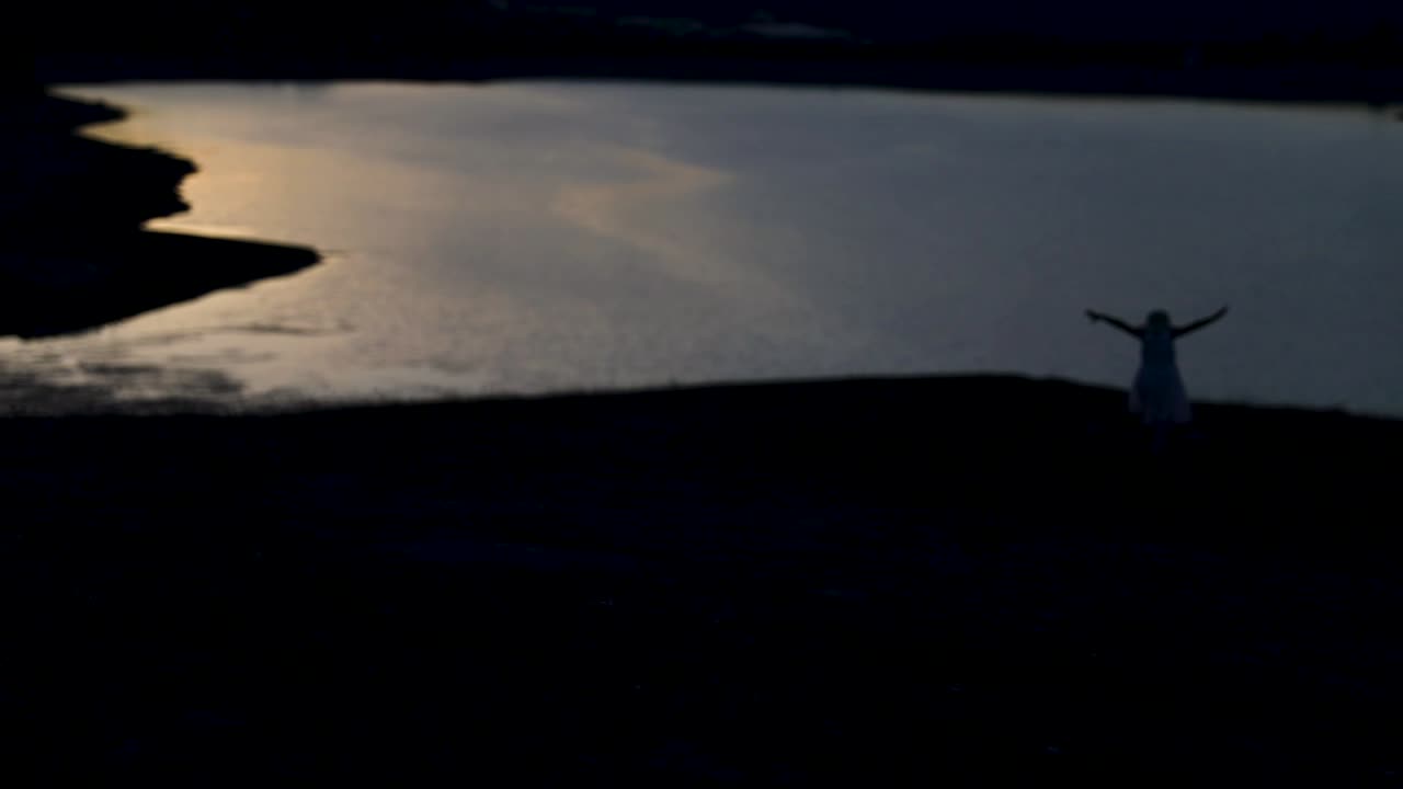 Girl in hat running with open hands at sunset with lake view.