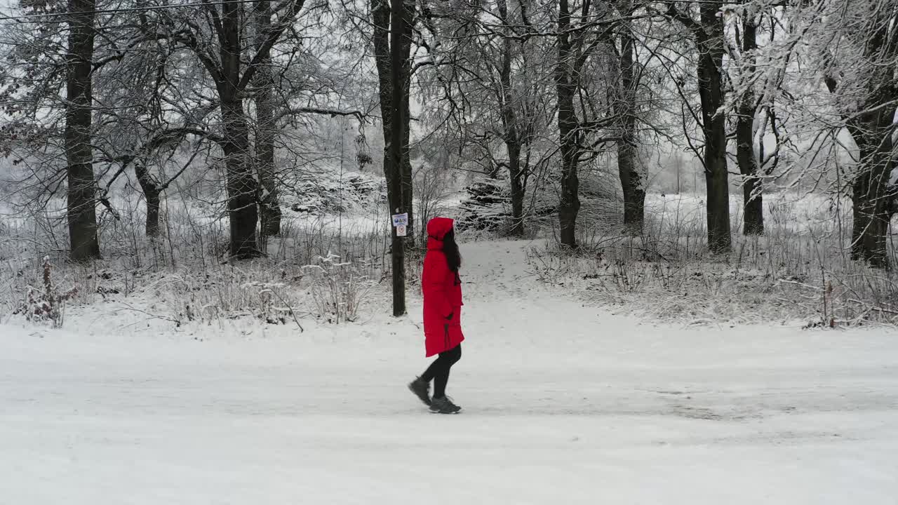 Donna caucasica con cappotto rosso cammina verso la foresta in un giorno d'inverno - vista laterale, carrellata.
