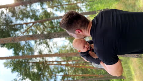 rear view of a man wearing a black t-shirt tossing his tiny infant baby. dad and son are in nature. vertical screen.