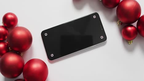 video of red christmas baubles and smartphone on white background