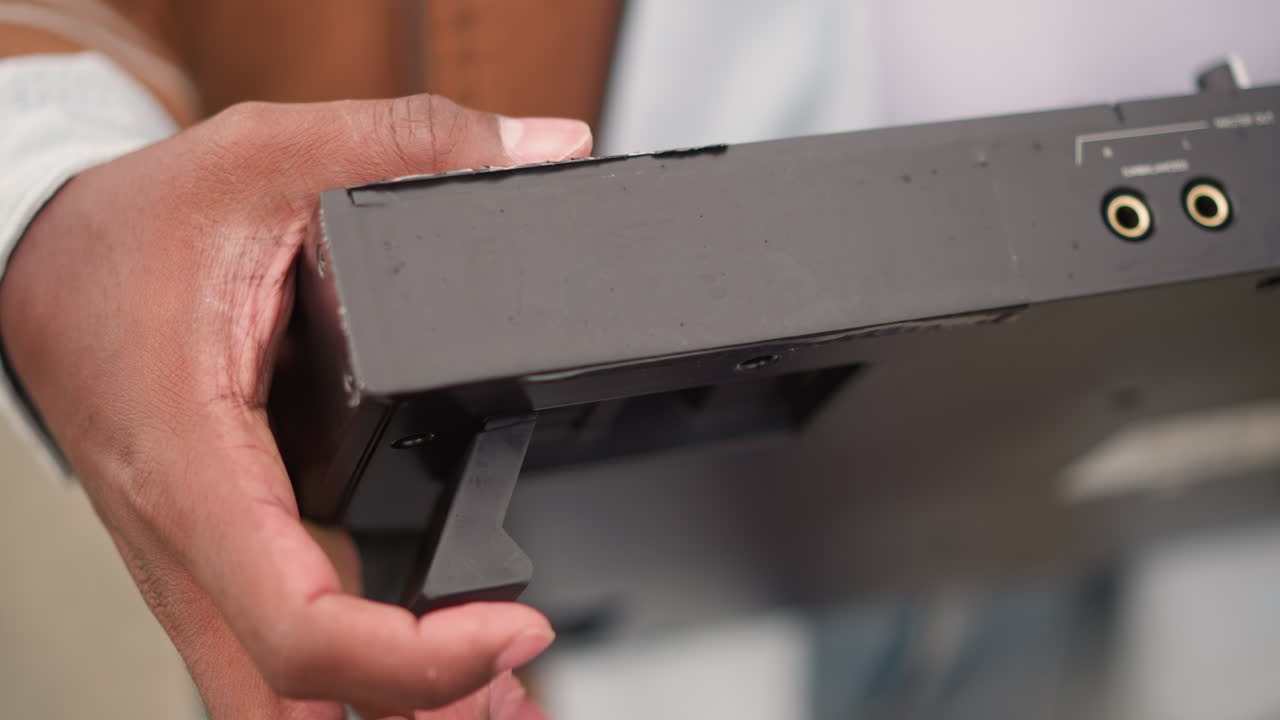 Mørke hænder justerer tastaturets støttefod på en bærbar controller, tekstureret metalhus og taktile fingerspidser forbereder sig på udendørs gadepark, oprigtig urban energi og varmt naturligt lys.