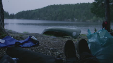 view from inside camp showing feet resting under tree canopy with canoe and lake in the background during light rainfall