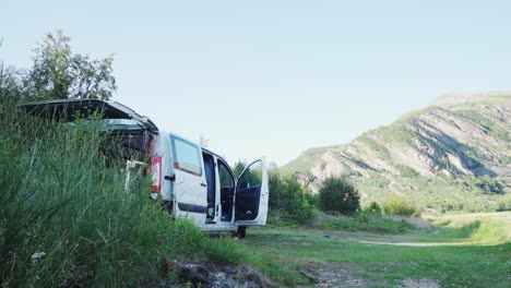 A-White-Campervan-With-Open-Doors-Parked-In-Grass-Field-Next-To-A-Mountain-In-Steigen,-Nordland-County,-Norway