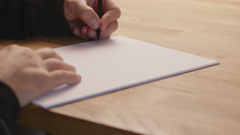 medio disparo de cerca de la escritura en una hoja de papel con la mano izquierda usando un lápiz