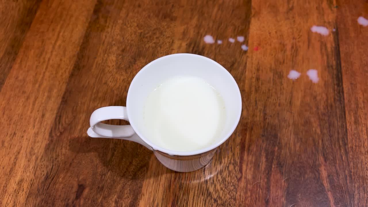 Xícara de leite com mãos de criança molhando um biscoito em uma mesa de madeira
